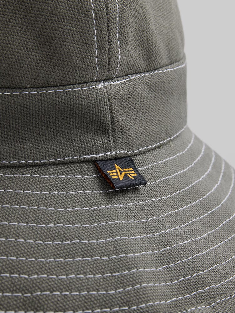Alpha Industries Canvas Daisy Mae MA-1 Bucket Hat, green canvas with white stitching, geometric black and yellow tag.