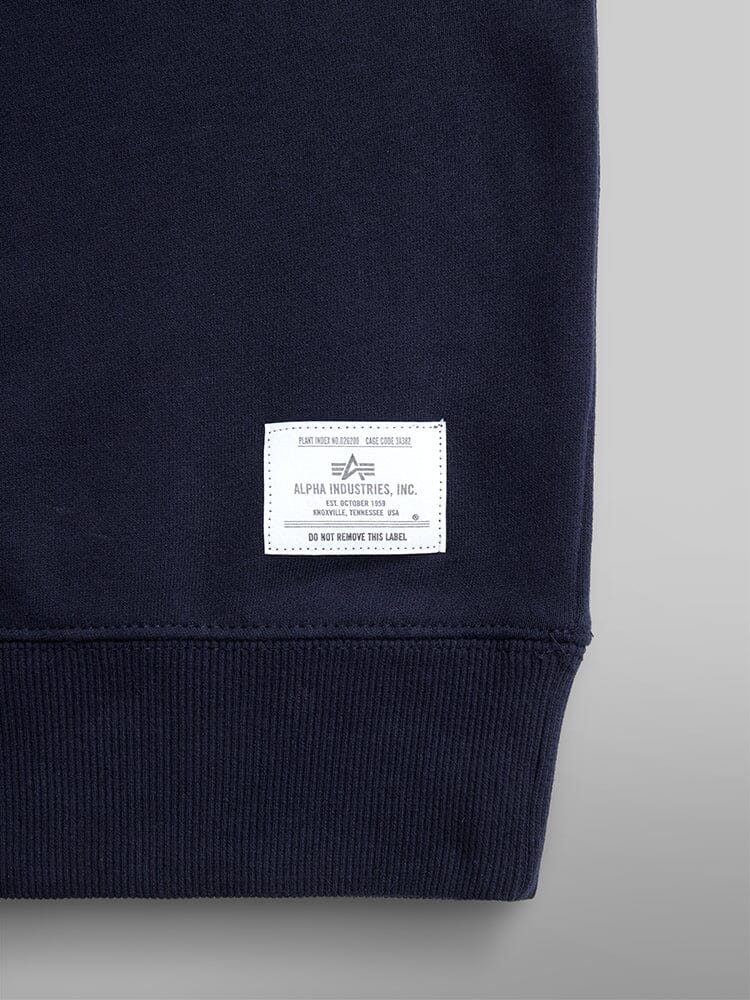 Close-up of a dark blue Essential Crewneck Sweater by Alpha Industries, featuring a white logo sewn onto the cotton-blend fabric.