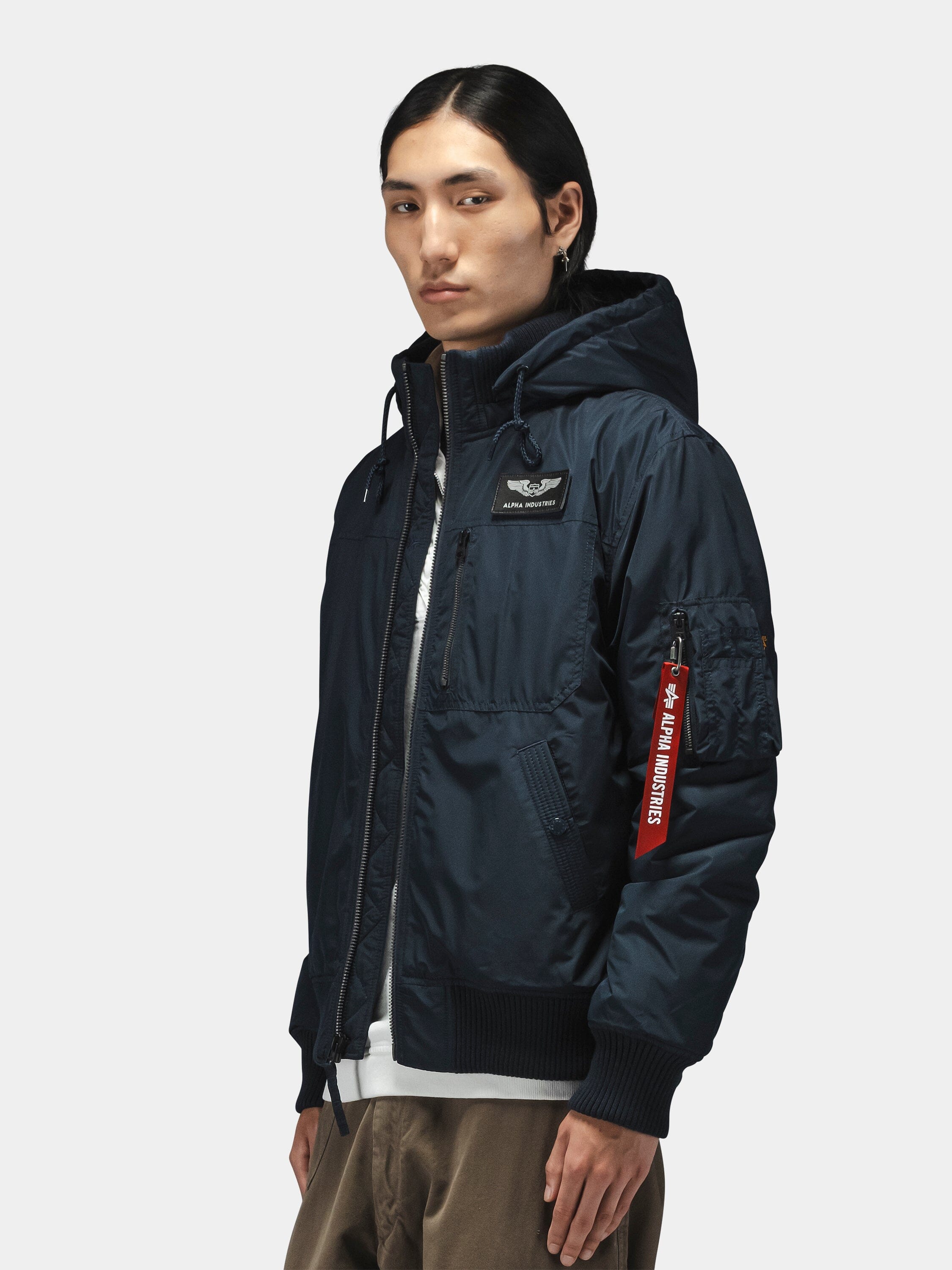 Alpha Industries Hooded Rib Flight Jacket in navy with utility sleeve pocket and "Remove Before Flight" tag.