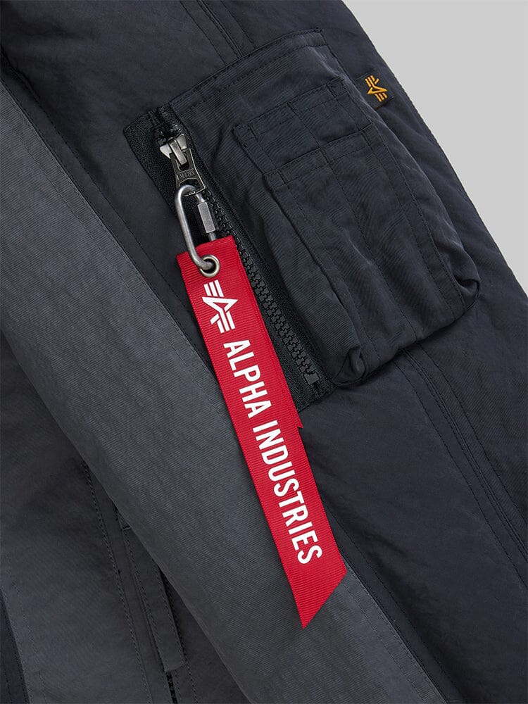 Close-up of the Insulated MA-1 Bomber Jacket in a dark color, showcasing its zippered pocket and distinctive red Alpha Industries tag affixed to a silver clip. The design is crafted from water-resistant fabric, perfectly blending style and functionality.
