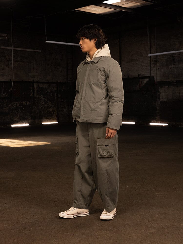 A person wearing an Alpha Industries Insulated Shirt Jacket and cargo pants stands in a dimly lit room with industrial walls and overhead lights, epitomizing the streetwear look.