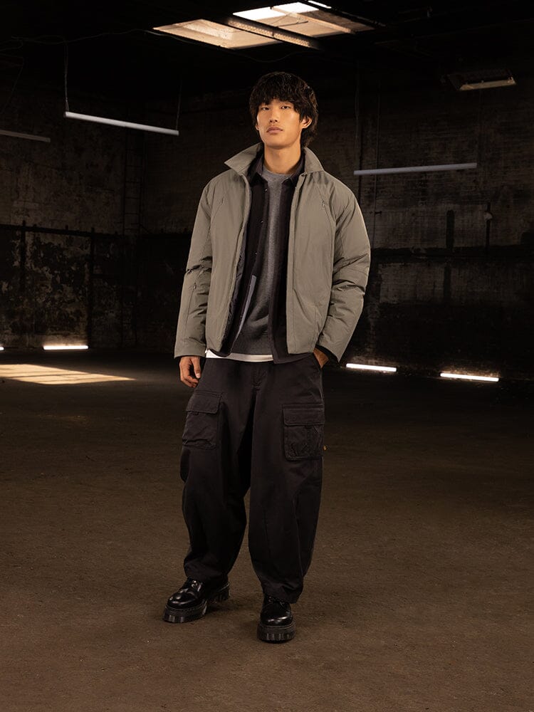 A person stands wearing the Insulated Shirt Jacket from Alpha Industries, paired with dark pants and black shoes, effortlessly pulling off a stylish streetwear look.