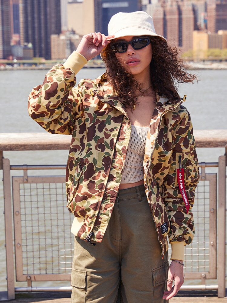 A person sporting the Alpha Industries, Inc. L-2B Hooded Gen II Bomber Jacket, along with khaki pants, sunglasses, and a white bucket hat, is highlighting their style with this lightweight hooded jacket.