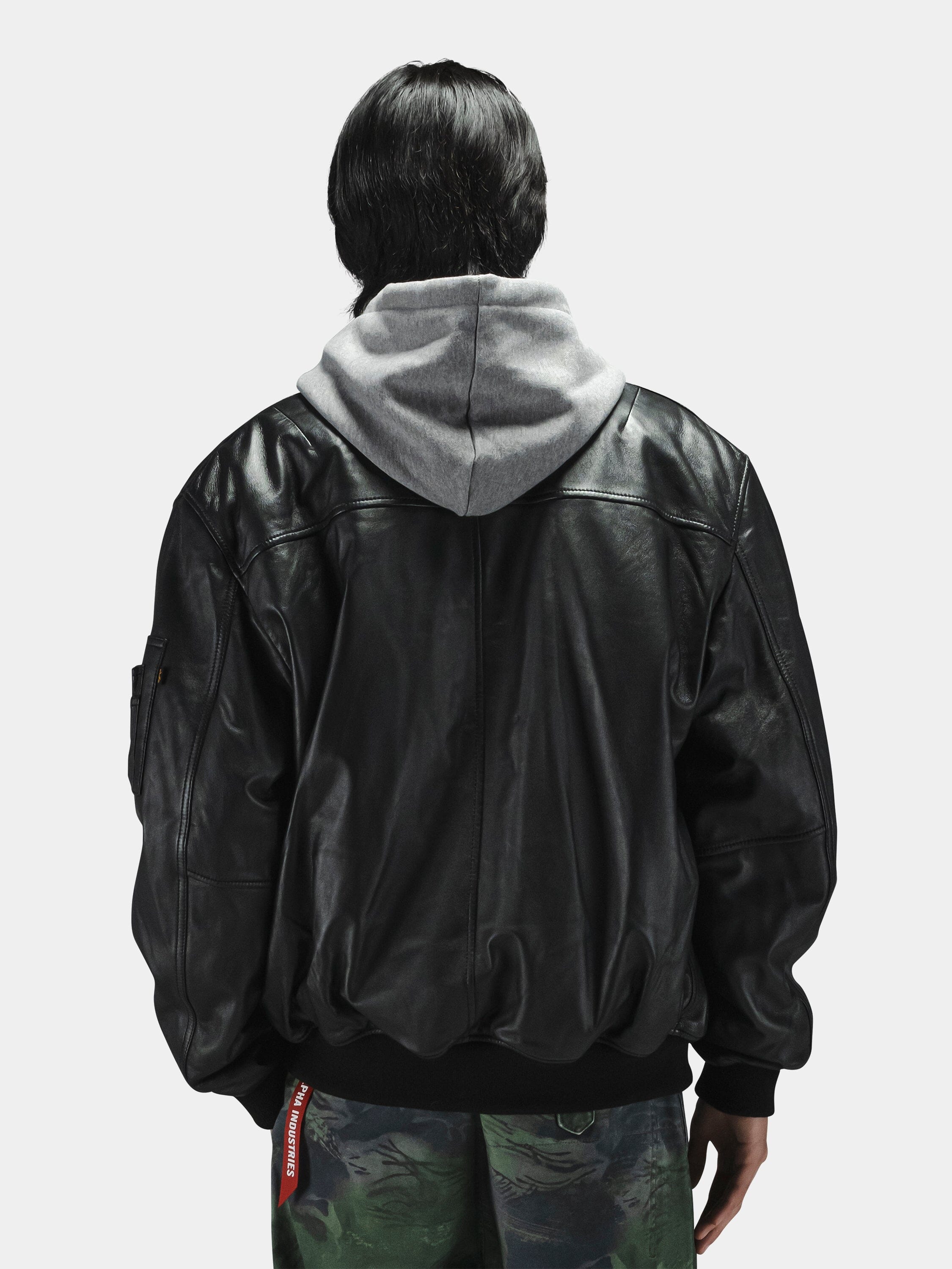 Alpha Industries Leather MA-1 Flight Jacket in black, layered over a gray hoodie and camouflage pants.