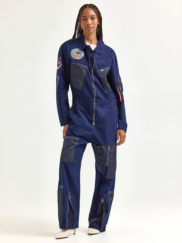 An individual wears the Alpha X Lee Flight Suit by Alpha Industries, showcasing its blue ripstop cotton design with patches and zippers.