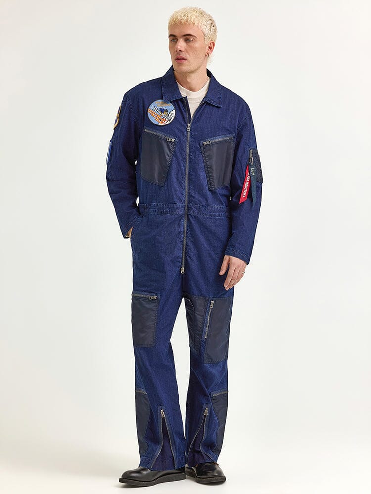 A person is standing wearing the Alpha X Lee Flight Suit by Alpha Industries, a blue jumpsuit crafted from ripstop cotton and embellished with various patches.