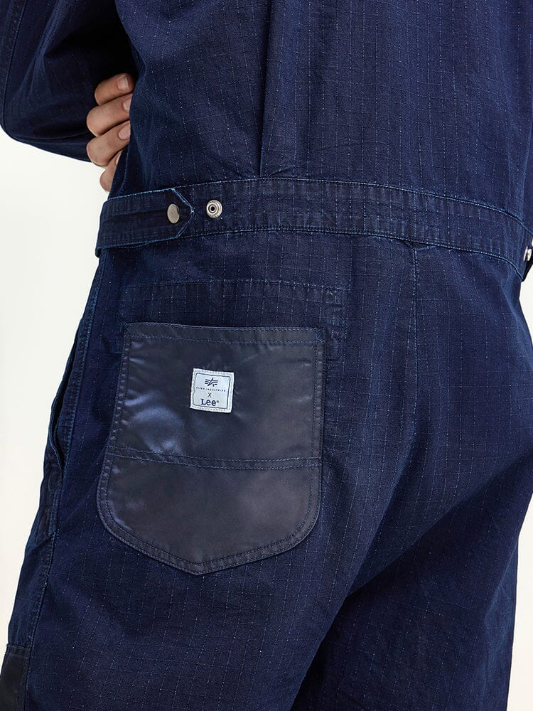 Close-up of a person wearing the Alpha X Lee Flight Suit, designed by Alpha Industries. This dark blue jumpsuit is crafted from ripstop cotton and features a front pocket with a small white logo patch.