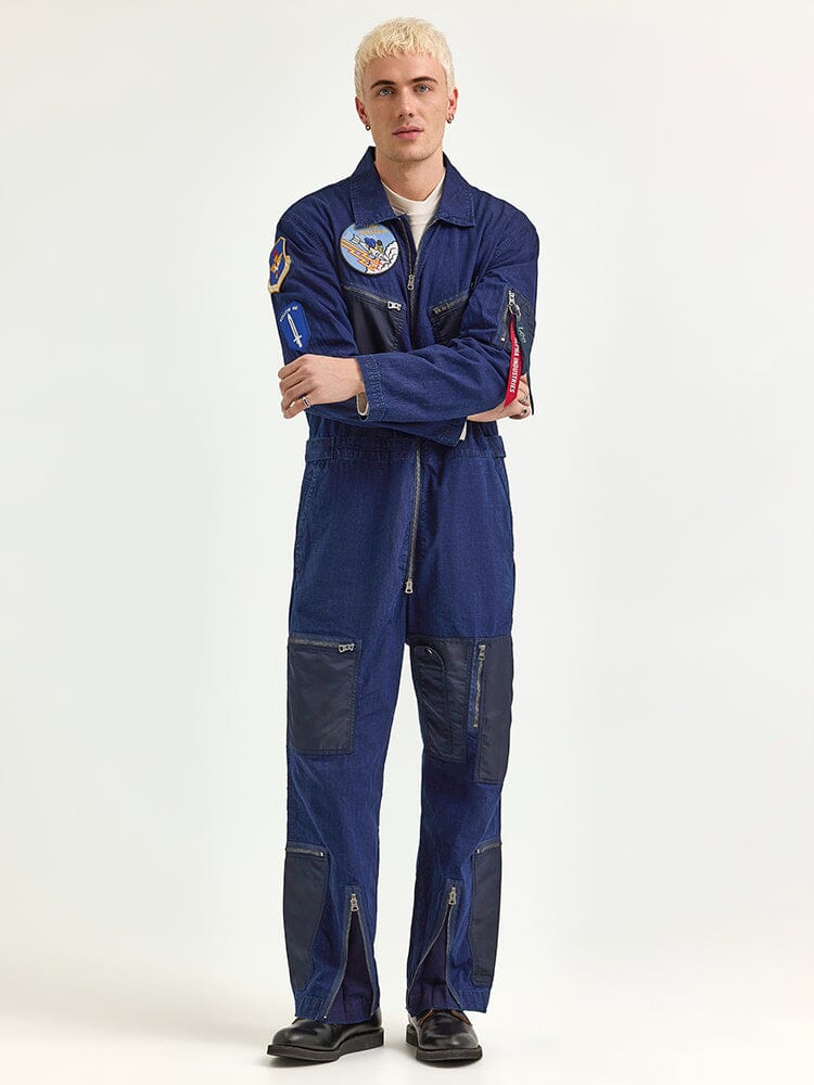 A person wearing the Alpha X Lee Flight Suit by Alpha Industries, featuring ripstop cotton in blue with patches and zippers, epitomizing performance fashion.