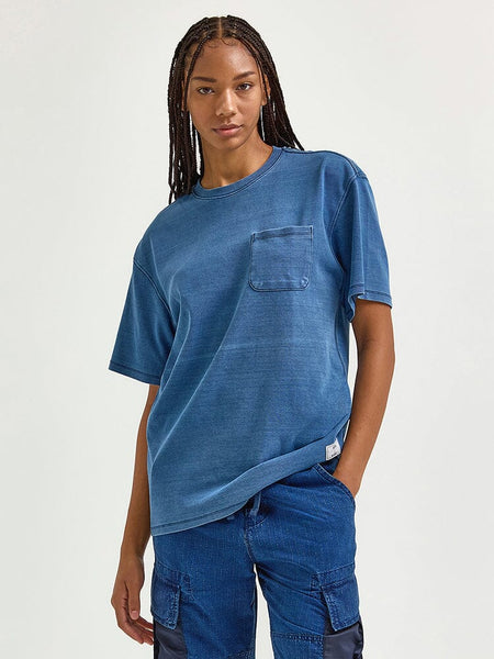 A person with long braids stands gracefully, wearing an Alpha Industries Fw24-Lee Looser Fit Indigo Dyed Tee in a soothing blue hue and pants featuring an indigo-dyed finish with a reinforced pocket.