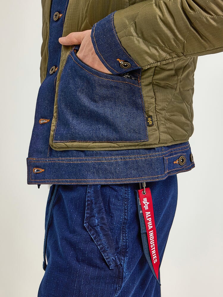 An individual is wearing an Alpha X Lee Quilted Jacket by Alpha Industries, featuring a red Alpha Industries tag on the side. This jacket expertly merges heritage style with timeless elements.