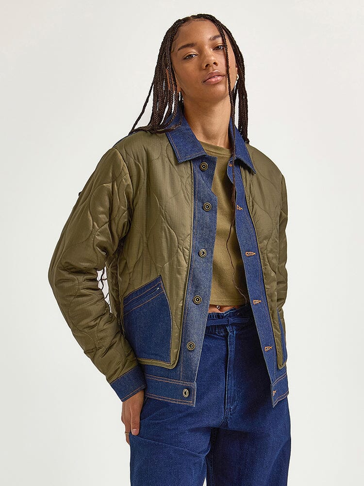 Wearing the Alpha X Lee Quilted Jacket from Alpha Industries, a person highlights a mixed-media design featuring quilted fabric and denim accents, seamlessly paired with jeans.