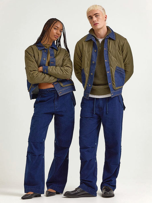 A woman and a man pose in matching heritage-style outfits: Alpha Industries' Alpha X Lee Quilted Jackets in OG-107 green with blue trim, paired with coordinating blue pants.