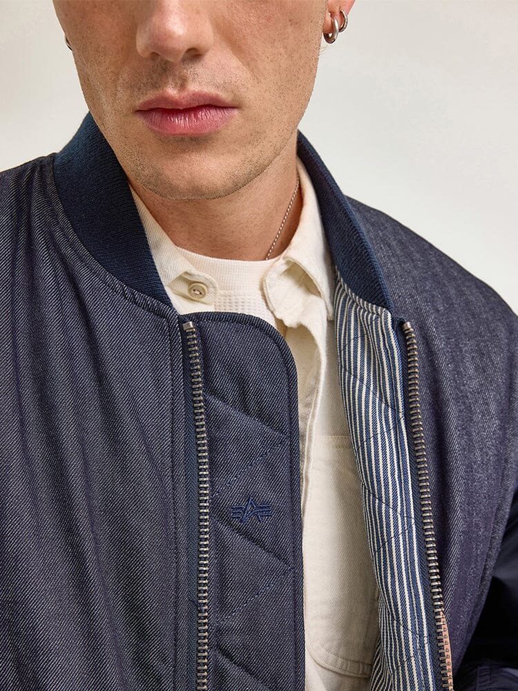 A person wearing the Alpha X Lee Reversible MA-1 Jacket by Alpha Industries over a button-up shirt.
