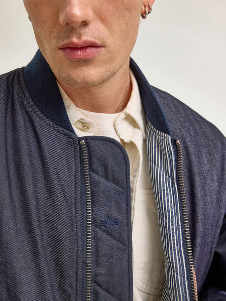 A person wearing the Alpha X Lee Reversible MA-1 Jacket by Alpha Industries over a button-up shirt.