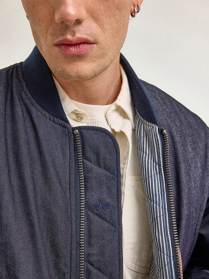 A person wearing the Alpha X Lee Reversible MA-1 Jacket by Alpha Industries over a button-up shirt.