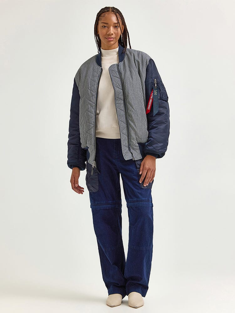 A person wearing an Alpha X Lee Reversible MA-1 Jacket over a white shirt, navy blue pants, and white shoes.