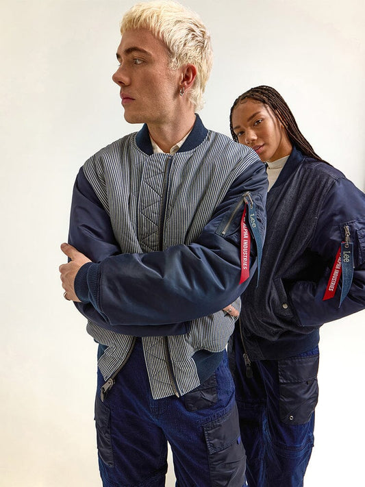 Two individuals wearing the Indigo Alpha X Lee Reversible MA-1 Jacket from Alpha Industries stand. One person faces left, while the other stands slightly behind, highlighting the versatility of this jacket.