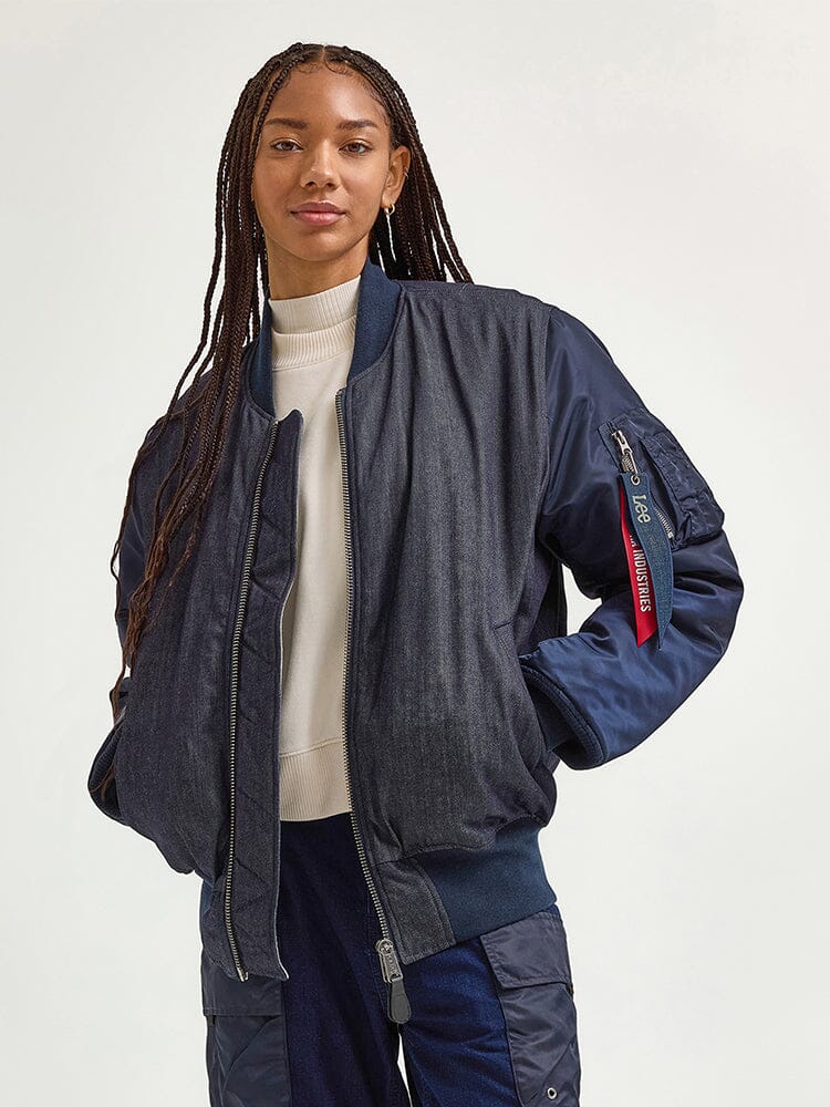 A person wearing an Alpha X Lee Reversible MA-1 Jacket from Alpha Industries and a white turtleneck stands with hands in pockets.