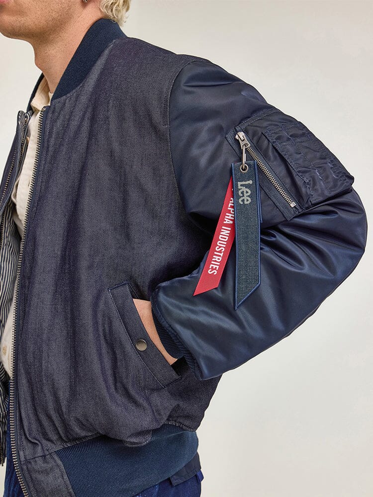 Sporting the Alpha X Lee Reversible MA-1 Jacket by Alpha Industries, this blue bomber jacket showcases a unique Remove Before Flight tag on the sleeve along with vintage railroad-stripe details, lending it a touch of classic charm.