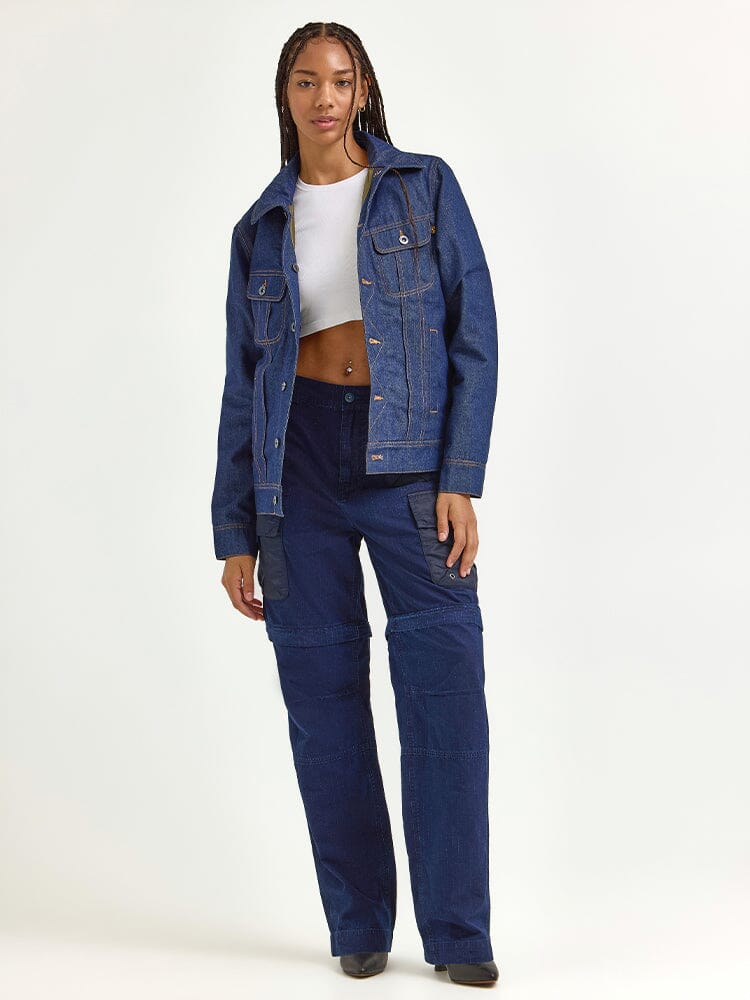 An individual confidently stands wearing a chic Alpha X Lee Reversible Rider Jacket from Alpha Industries, paired with matching pants and a white cropped top.