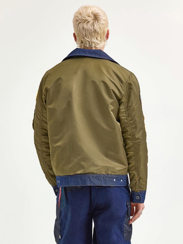 A person with short blond hair wearing the Alpha X Lee Reversible Rider Jacket from Alpha Industries and blue denim rider jeans, facing away.