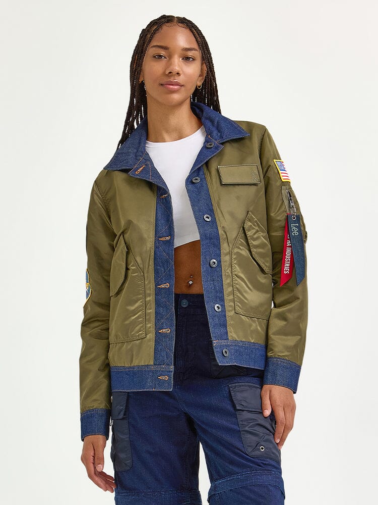 A person confidently stands wearing the stylish Alpha X Lee Reversible Rider Jacket by Alpha Industries, paired with a white crop top and dark pants.