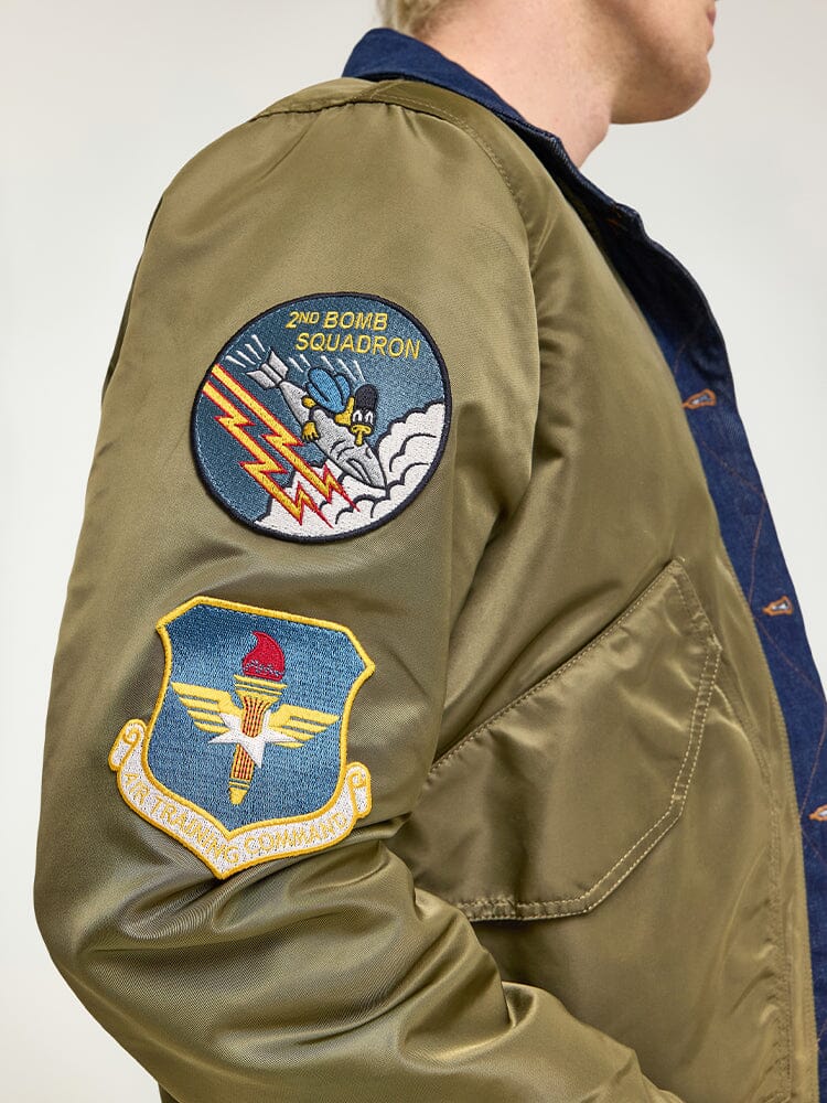 The individual is donning an Alpha X Lee Reversible Rider Jacket in green, featuring the 2nd Bomb Squadron patch and another patch on the sleeve, reminiscent of an Alpha Industries MA-1 flight jacket.