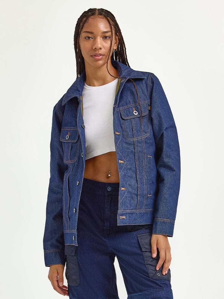 A person poses wearing the Alpha x Lee Reversible Rider Jacket by Alpha Industries, paired with a white crop top and dark blue pants.