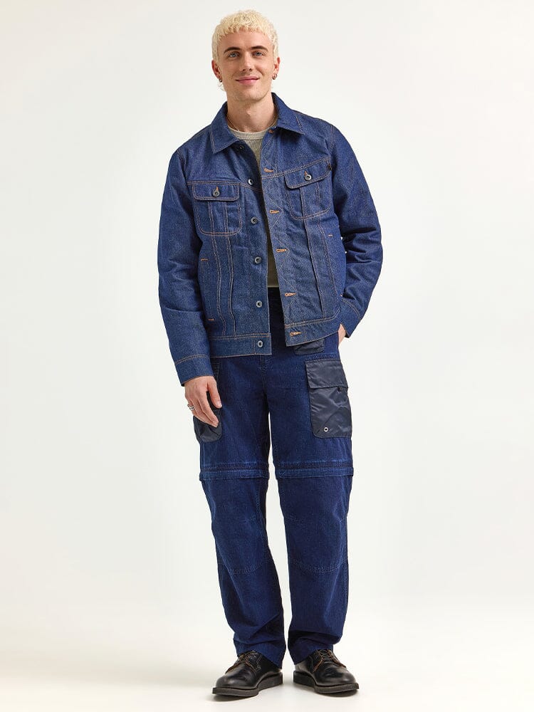 An individual wearing an Alpha X Lee Reversible Rider Jacket and jeans, paired with black shoes.