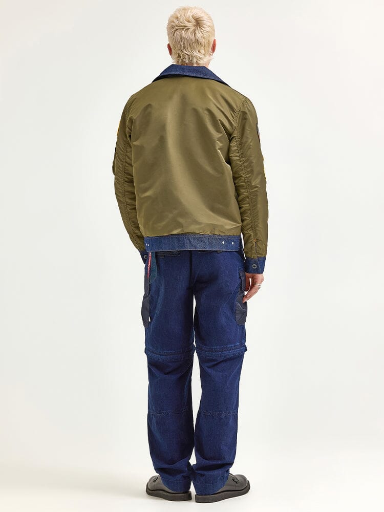 A person is wearing an Olive Green Alpha X Lee Reversible Rider Jacket by Alpha Industries and blue jeans, standing with their back to the camera.