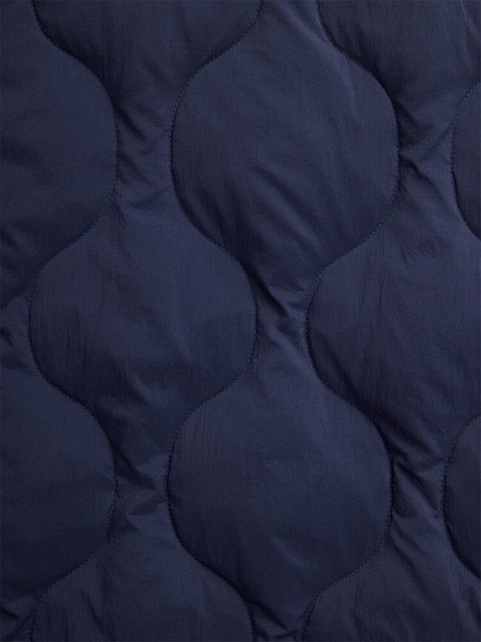 Close-up of the Lightweight Quilted Down Jacket by Alpha Industries, showcasing its dark blue fabric with a wave-like quilted pattern, providing a luxurious down-filled feel.