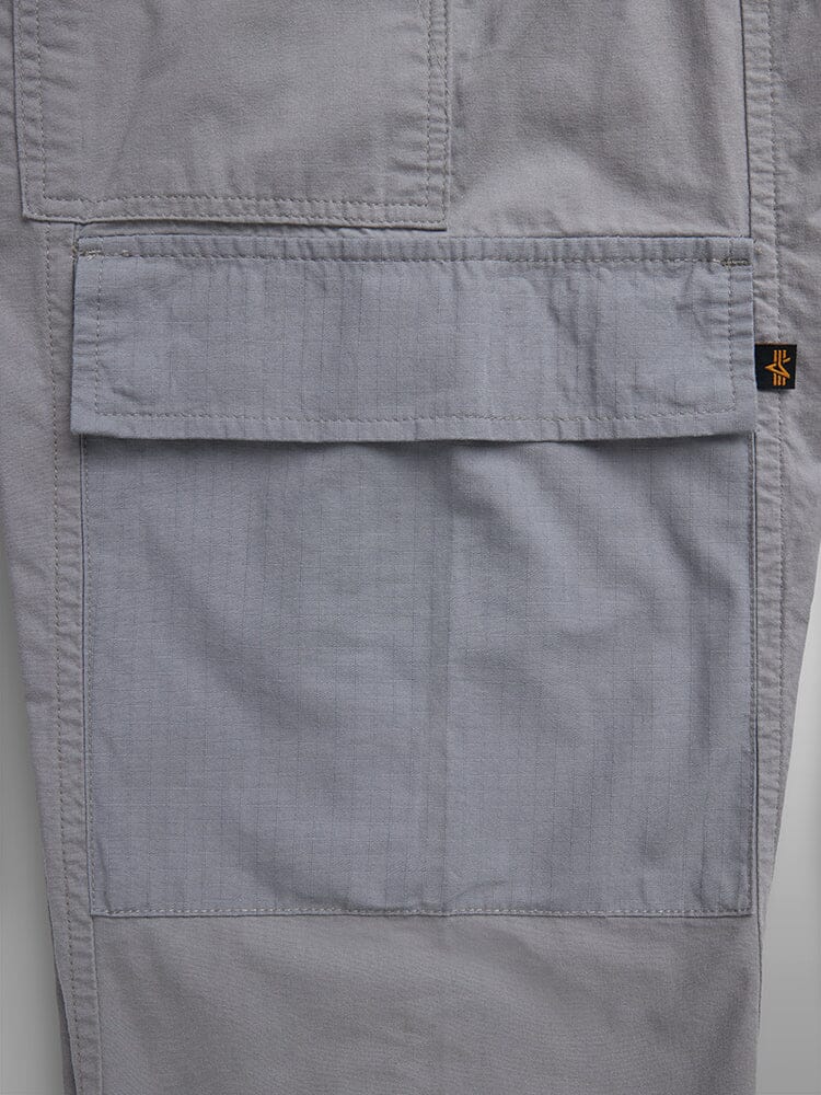 Lightweight Trouser W by Alpha Industries, gray, garment-washed cotton, cargo pocket with flap and visible stitching, small black and yellow tag.