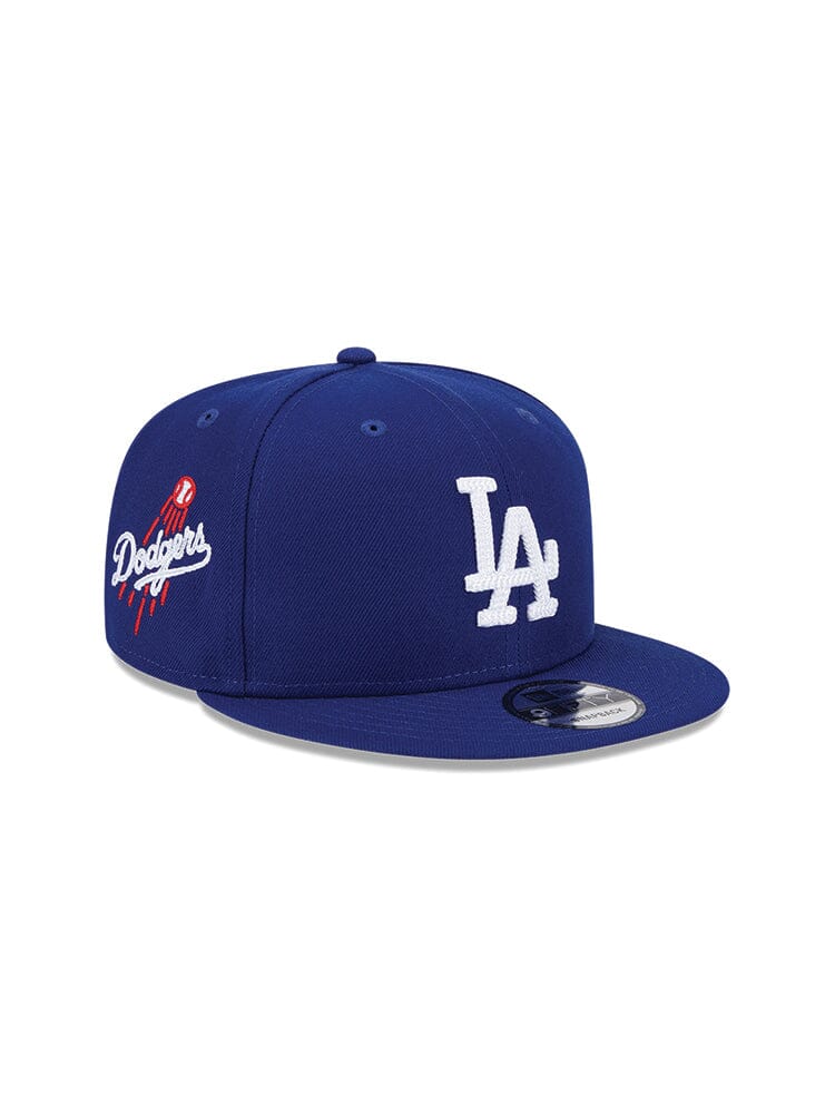 Introducing the Los Angeles Dodgers X Alpha X New Era 950 Cap (Blue) - a striking blue baseball cap showcasing a prominent white LA emblem on the front and a subtle Dodgers team logo with a baseball motif on the side. Created in partnership with Alpha Industries and New Era, this cap perfectly blends style and iconic appeal.