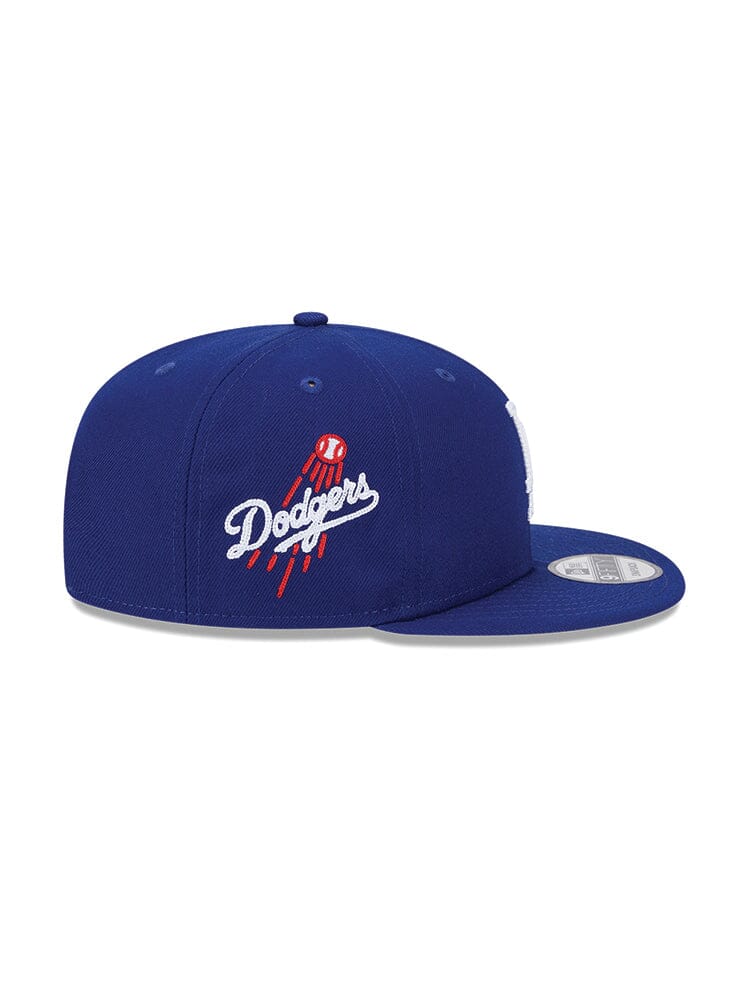 The Los Angeles Dodgers X Alpha X New Era 950 Cap (Blue) is a fashionable cap that showcases the Dodgers emblem alongside a striking red, white, and blue rocket design. It's ideal for fans looking to make a bold statement.