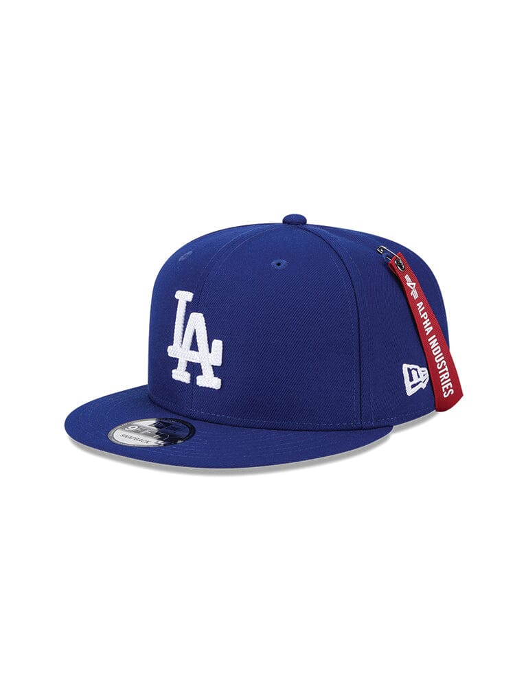 Discover the Los Angeles Dodgers x Alpha x New Era 950 Cap (Blue) by Alpha Industries, featuring a LA team logo in white on a dark blue 9FIFTY Snapback baseball cap. This exclusive piece showcases a flat brim and a unique red tag on the side, blending sporty style with top-notch craftsmanship.