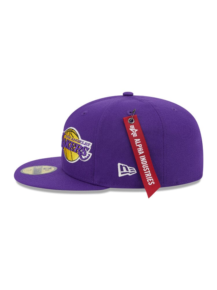 The Los Angeles Laker x Alpha x New Era 59Fifty Fitted Cap features a purple design displaying the Los Angeles Lakers team logo, accented by a unique red Alpha Industries tag.