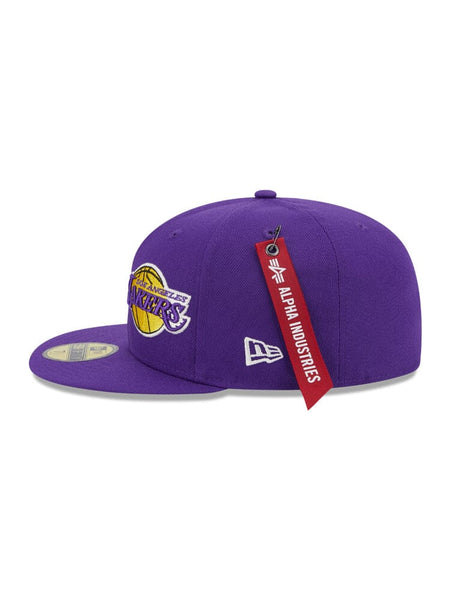 The Los Angeles Laker x Alpha x New Era 59Fifty Fitted Cap features a purple design displaying the Los Angeles Lakers team logo, accented by a unique red Alpha Industries tag.