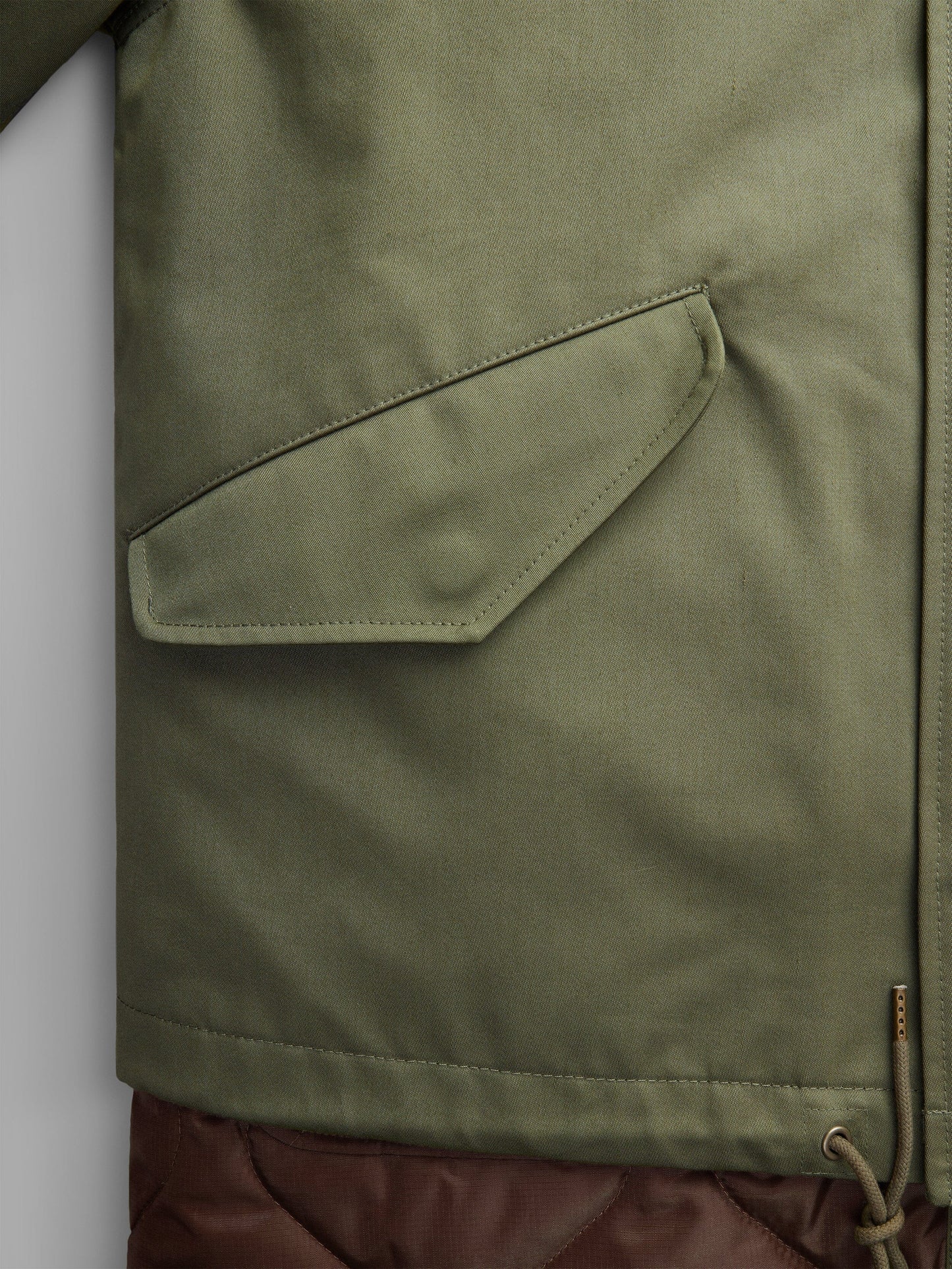 Close-up of the M-65 Long Liner, a green jacket by Alpha Industries, showcasing its NYCO fabrication with a side pocket and an onion quilted lower section for enhanced style.