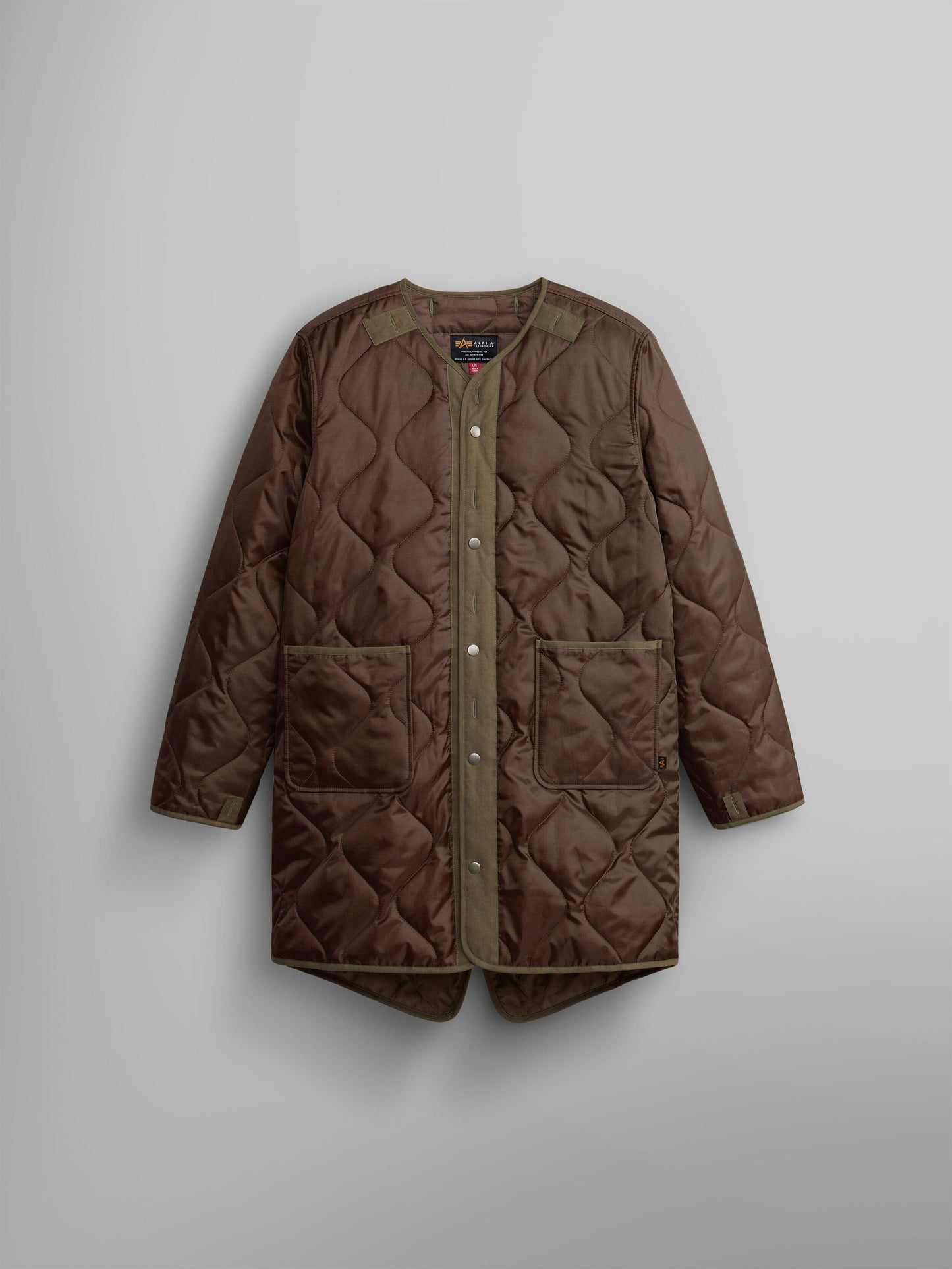 The M-65 Long Liner from Alpha Industries is a brown quilted jacket with snap buttons and two front pockets, featuring an onion quilted lining.
