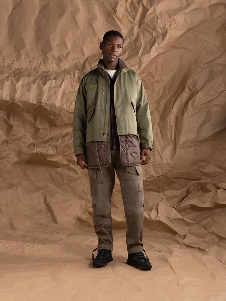 An individual is dressed in Alpha Industries' M-65 Long Liner in olive green.