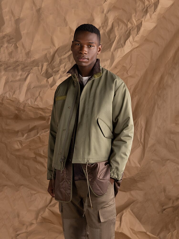 A person wearing the Alpha Industries M-65 Long Liner jacket in OG-107 Green.