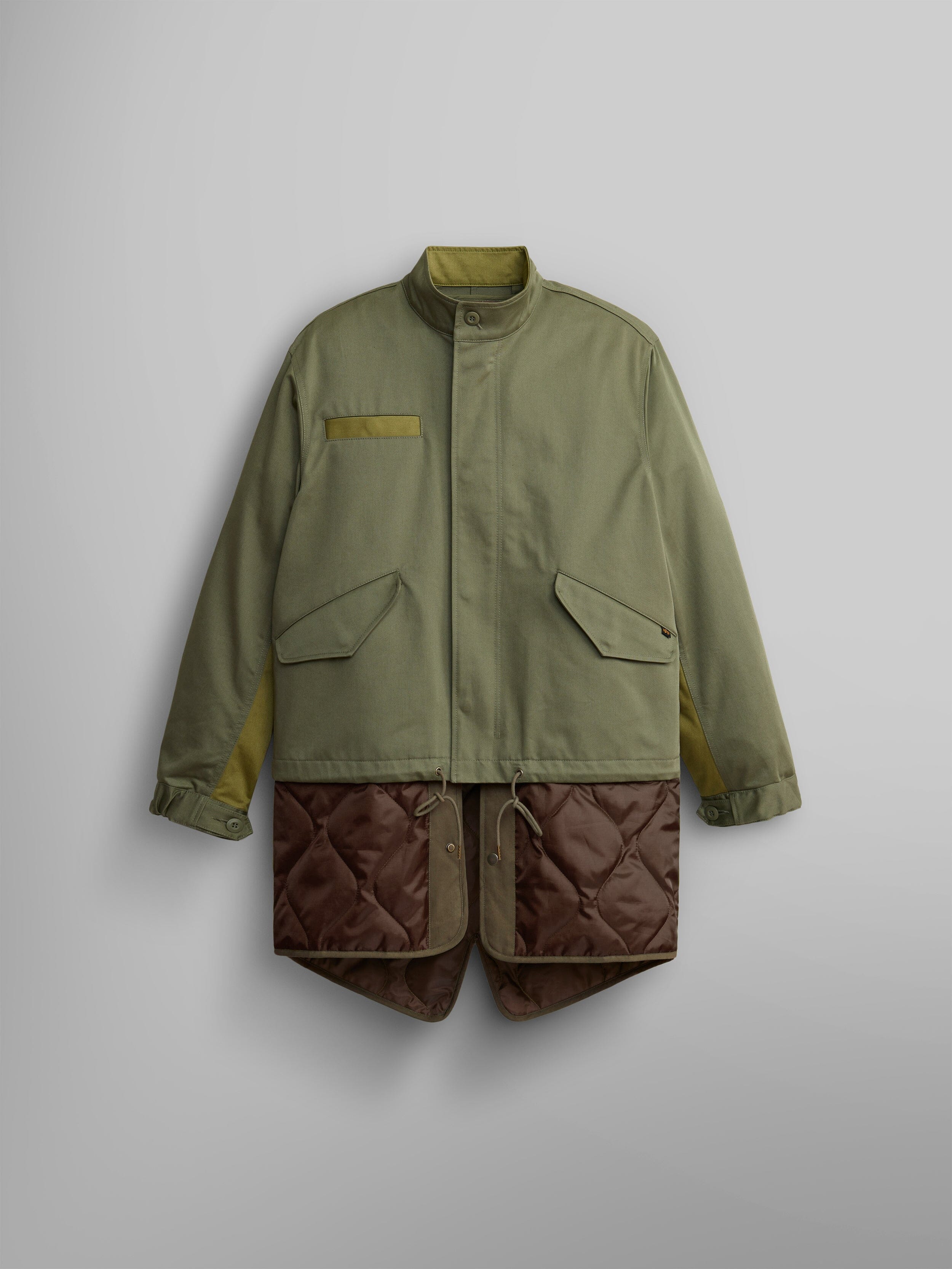 The M-65 Long Liner from Alpha Industries features a high collar and large pockets in OG-107 Green, elegantly displaying an onion quilted lining that extends from the hem.