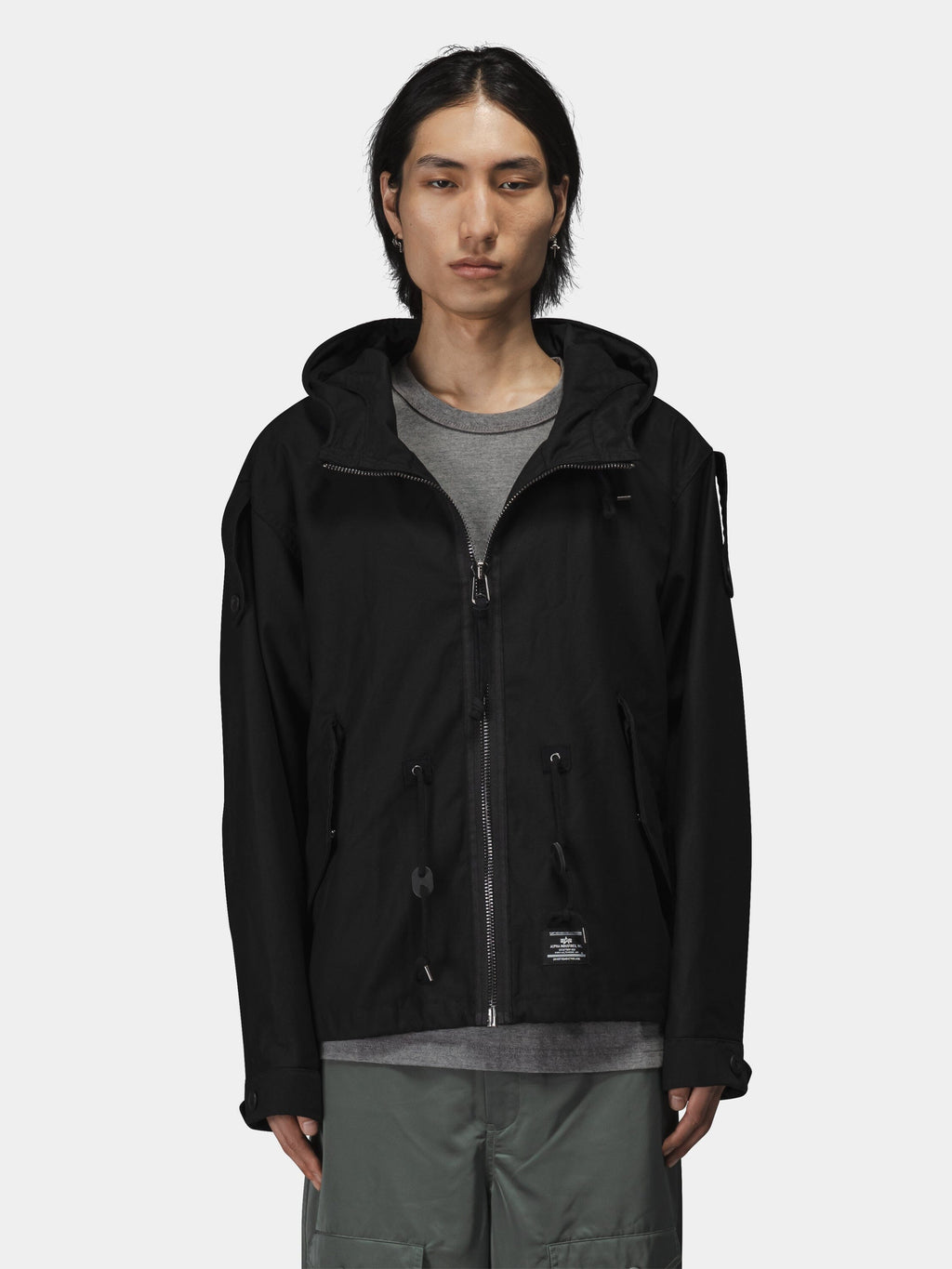 Alpha Industries M-65 Mod Fishtail Field Coat in dark material with fishtail hem over gray shirt and green pants.