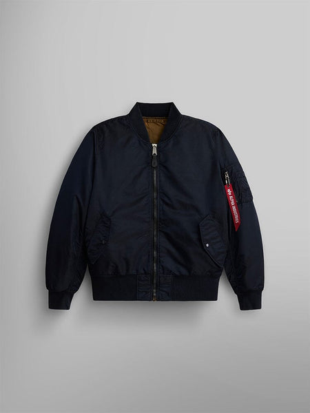 The MA-1 Battlewash Bomber Jacket by Alpha Industries, Inc. features a zippered front, striking orange interior lining, and a distinctive red tag on the left sleeve pocket. This reversible jacket in replica blue adds versatile style to your wardrobe.