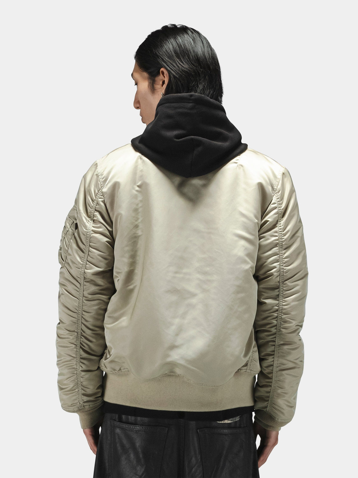 Alpha Industries MA-1 Bomber Jacket in beige, shiny material, worn over black hoodie and dark pants.