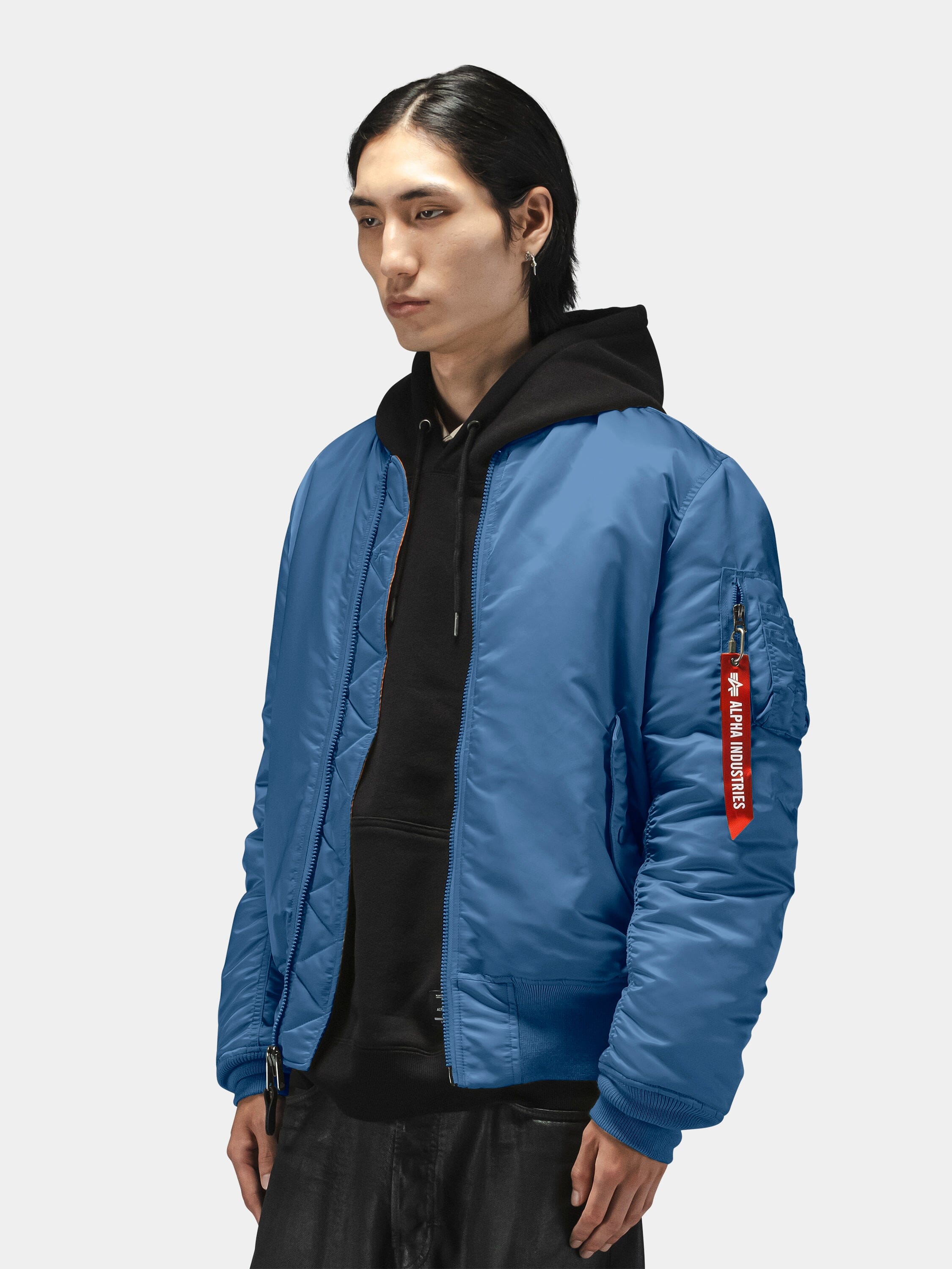 Alpha Industries MA-1 Bomber Jacket in blue with red sleeve tag, worn over black hoodie.