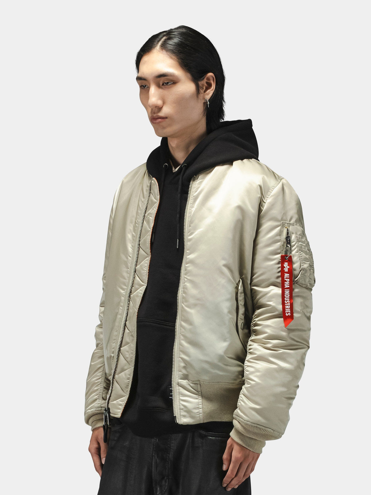 Alpha Industries MA-1 Bomber Jacket in light beige with black hoodie, featuring zip closure and ribbed cuffs.
