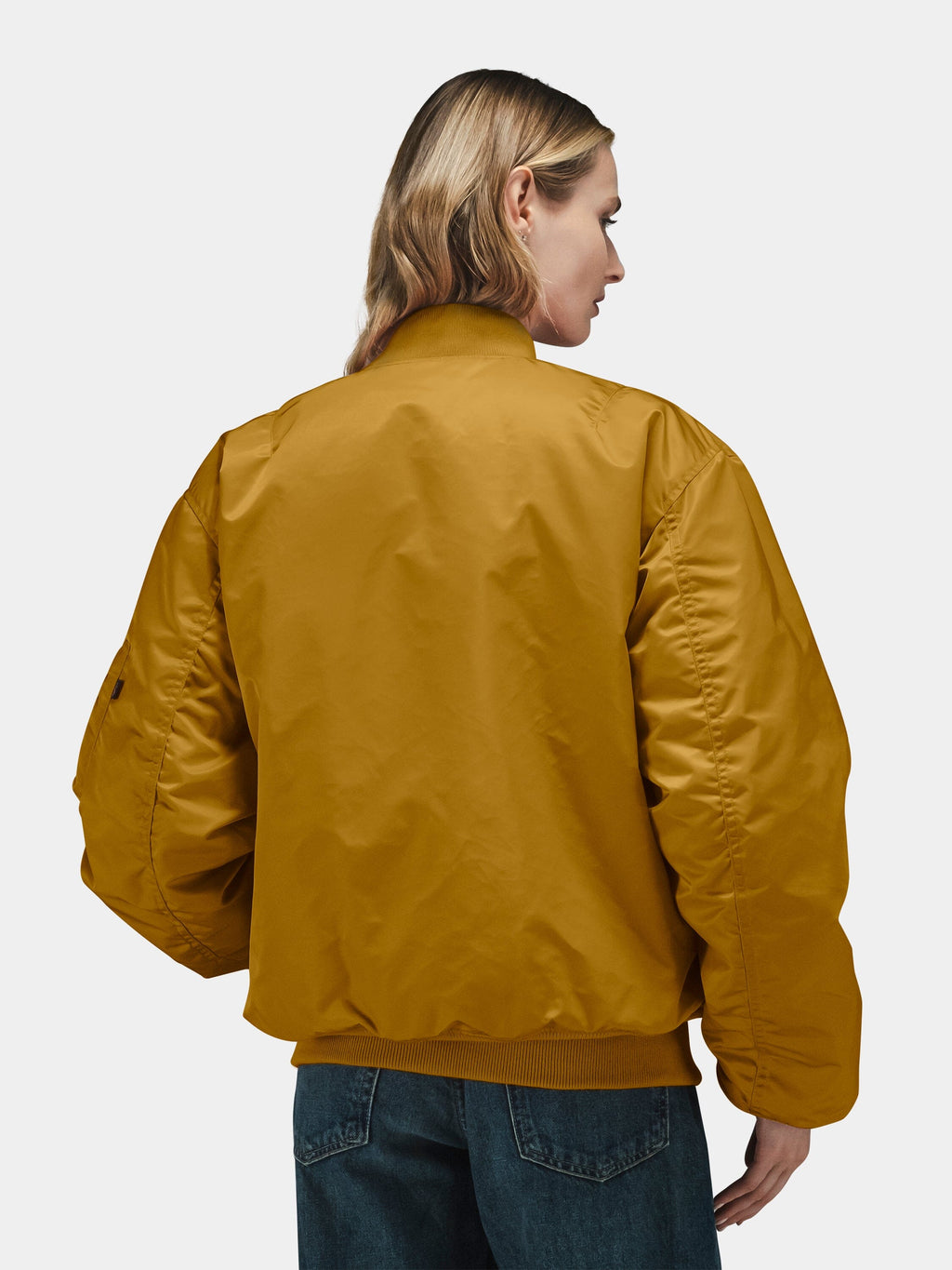 Mustard yellow Alpha Industries MA-1 Bomber Jacket with front zip closure, ribbed cuffs and hem, paired with blue jeans.