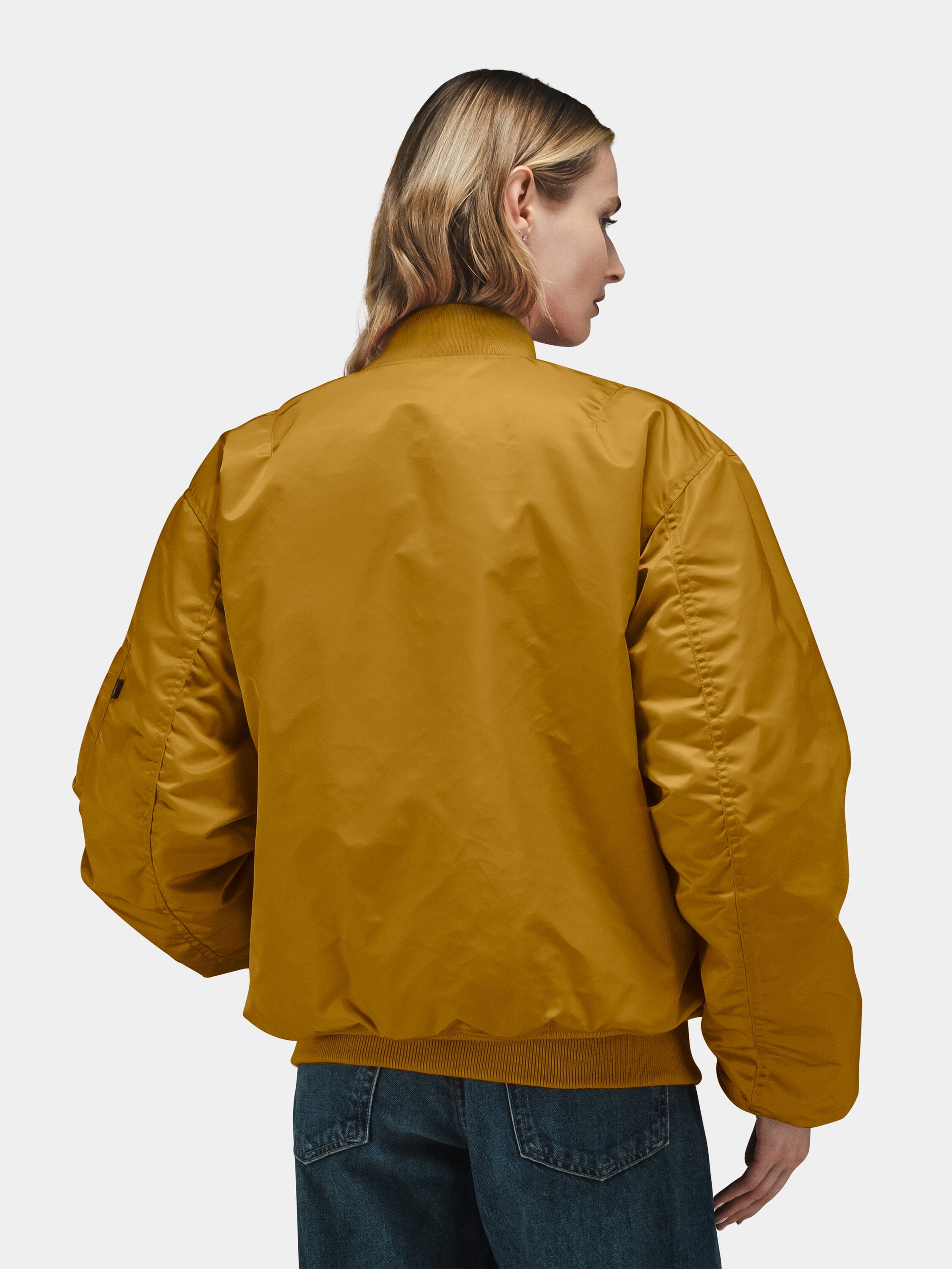 Mustard yellow Alpha Industries MA-1 Bomber Jacket with front zip closure, ribbed cuffs and hem, paired with blue jeans.