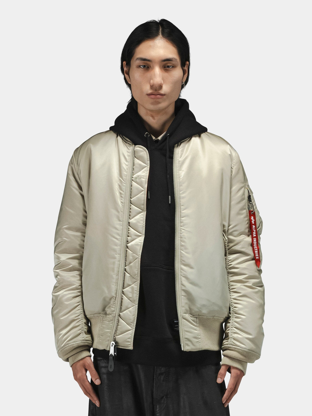 Alpha Industries MA-1 Bomber Jacket, light color, worn over black hoodie; visible ribbed cuffs and zip closure.